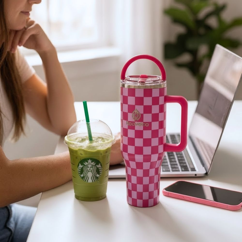 Pink checkered Rooveco tumbler on a desk beside a laptop and iced drink. Clean workspace lifestyle scene.