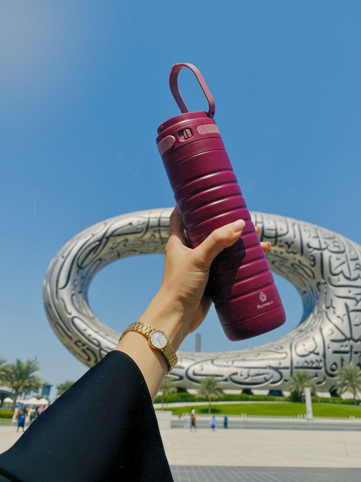 Hand holding a berry-colored Rooveco tumbler in front of the Museum of the Future in Dubai. Premium lifestyle product shot.